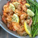 Lemon garlic shrimp and whole asparagus in a light gray skillet with parsley and lemon wedges