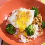 Teriyaki chicken and broccoli rice bowl topped with a fried egg and crispy onions