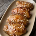 Whole sesame chicken thighs with glossy honey-soy glaze and sesame seeds on a long ceramic platter