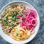 Mediterranean lentils and rice in a shallow bowl with pink pickled onions, hummus, and parsley