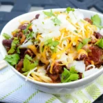 Bowl of Cincinnati chili with kidney beans, shredded cheddar, diced white onion, and cilantro