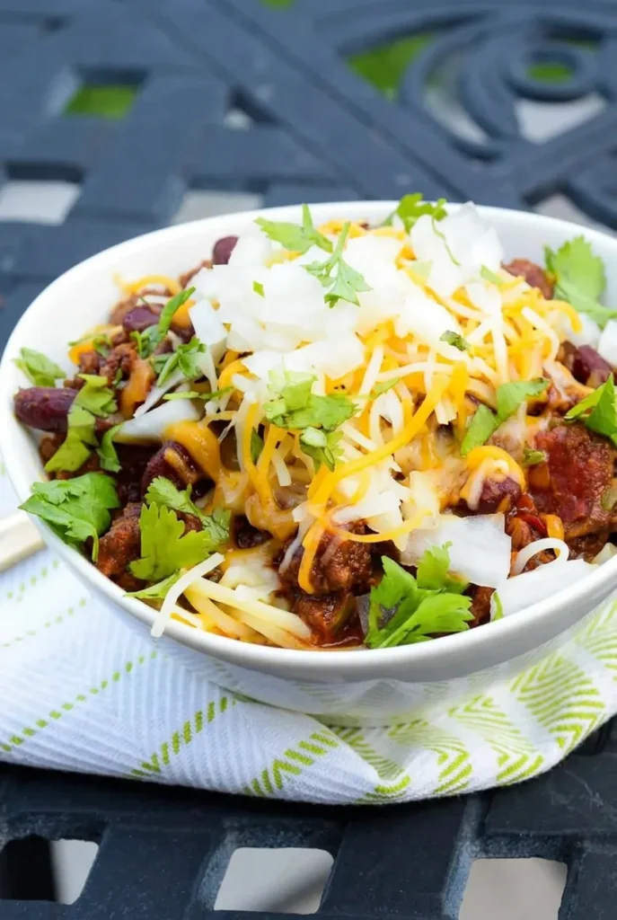 Bowl of Cincinnati chili with kidney beans, shredded cheddar, diced white onion, and cilantro