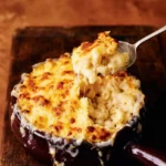 Classic baked mac and cheese in a deep burgundy dish, with a creamy serving lifted through strands of melted cheese