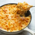 Southern baked mac and cheese in a white skillet, with a soft scoop lifted from its browned cheese top