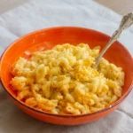 Creamy four cheese elbow macaroni piled in a shallow orange bowl with a serving spoon