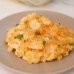 Loose scoop of baked Velveeta mac and cheese with golden crumbs and parsley on a warm beige plate