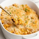 Baked gluten-free mac and cheese in a white casserole dish, with golden crumbs, chives and a lifted spoonful