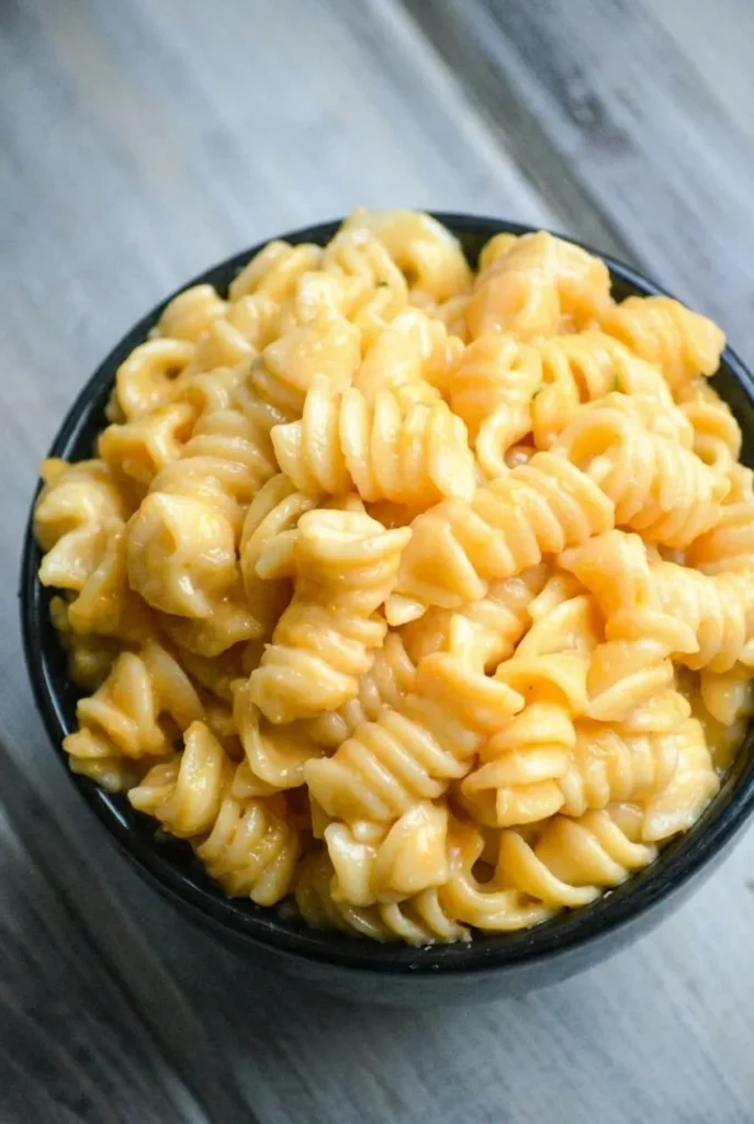 Heaped dark bowl of Instant Pot rotini mac and cheese coated in glossy golden sauce