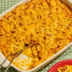 No-roux mac and cheese in a rectangular baking dish, with a browned cheddar top and creamy shells exposed at one edge