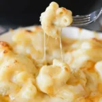 Gouda mac and cheese in a shallow baking dish, with a fork lifting a bite and strands of melted cheese
