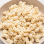 Shallow beige bowl of glossy white cheddar mac and cheese with curved cavatappi