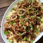 Italian mac and cheese in a white serving dish with browned sausage, fried onion rings, and scallions