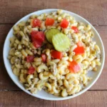 Cheeseburger mac and cheese on a white plate with diced tomato and overlapping dill pickle chips