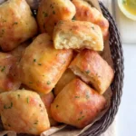 Garlic butter rolls piled in a parchment-lined basket, with parsley-flecked tops and one opened to show its fluffy crumb