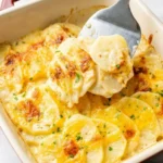 Cheesy scalloped potatoes in a ceramic dish, with creamy overlapping slices lifted on a spatula