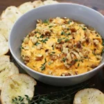 Pumpkin whipped feta dip topped with walnuts and thyme in a gray bowl, with sliced baguette alongside
