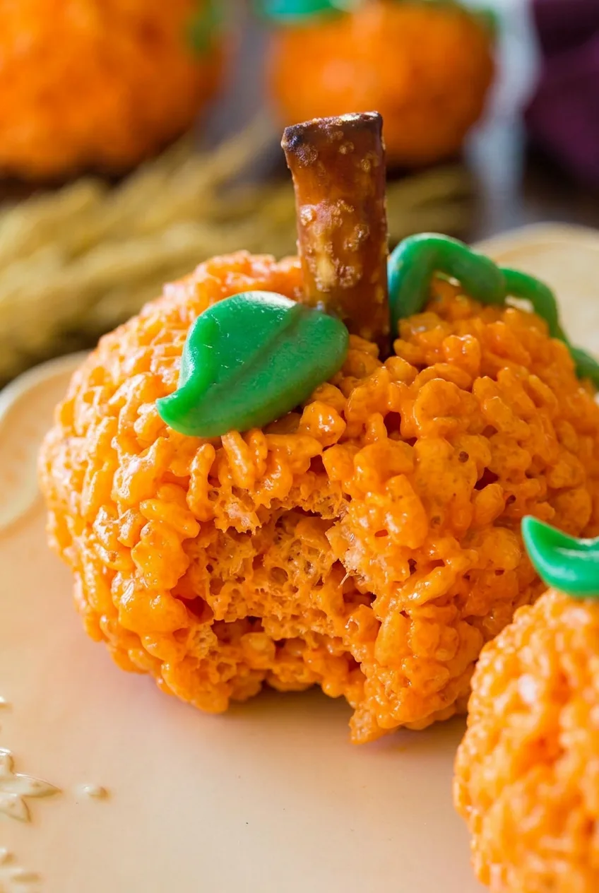Close view of a Pumpkin Rice Krispie Treat showing glossy puffed-rice texture, pretzel stem, and green icing vine.