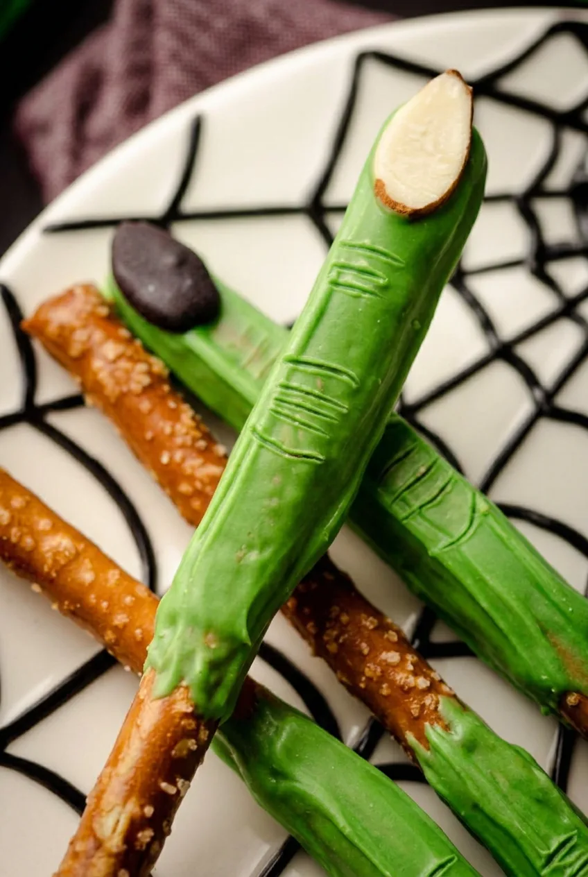Close view of a green witch finger pretzel rod with almond nail and knuckle wrinkles.