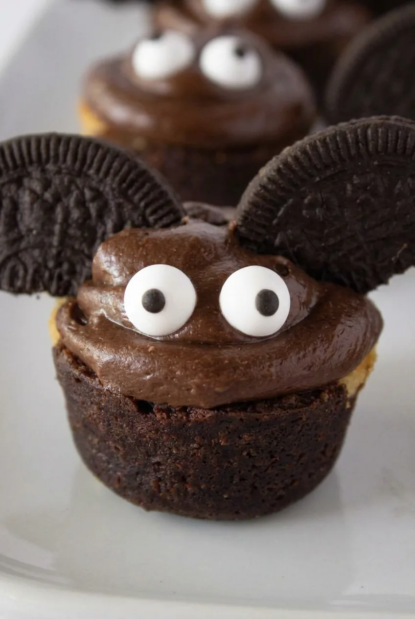 Close view of a Halloween brownie bat showing glossy chocolate frosting, candy eyes, and embossed cookie wings.