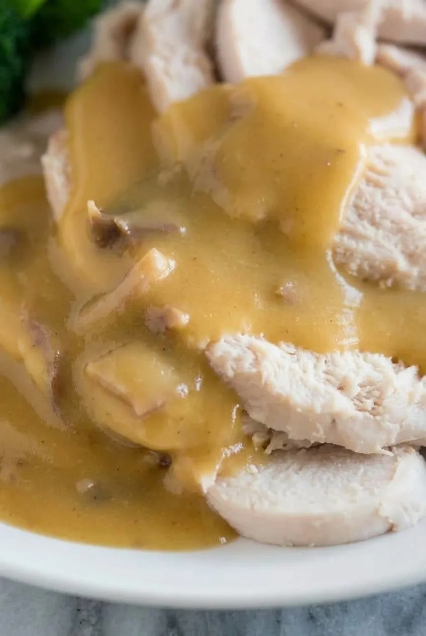 Close view of glossy turkey gravy coating tender sliced roast turkey with tiny roasted pan-bit flecks.