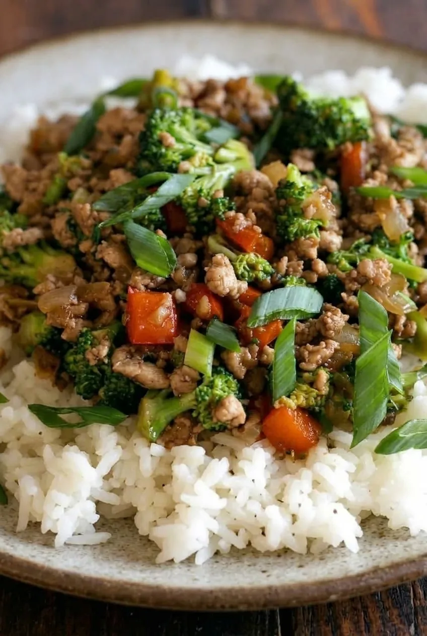 Close view of glossy ground turkey crumbles with broccoli, red pepper, scallions, and separate fluffy rice.