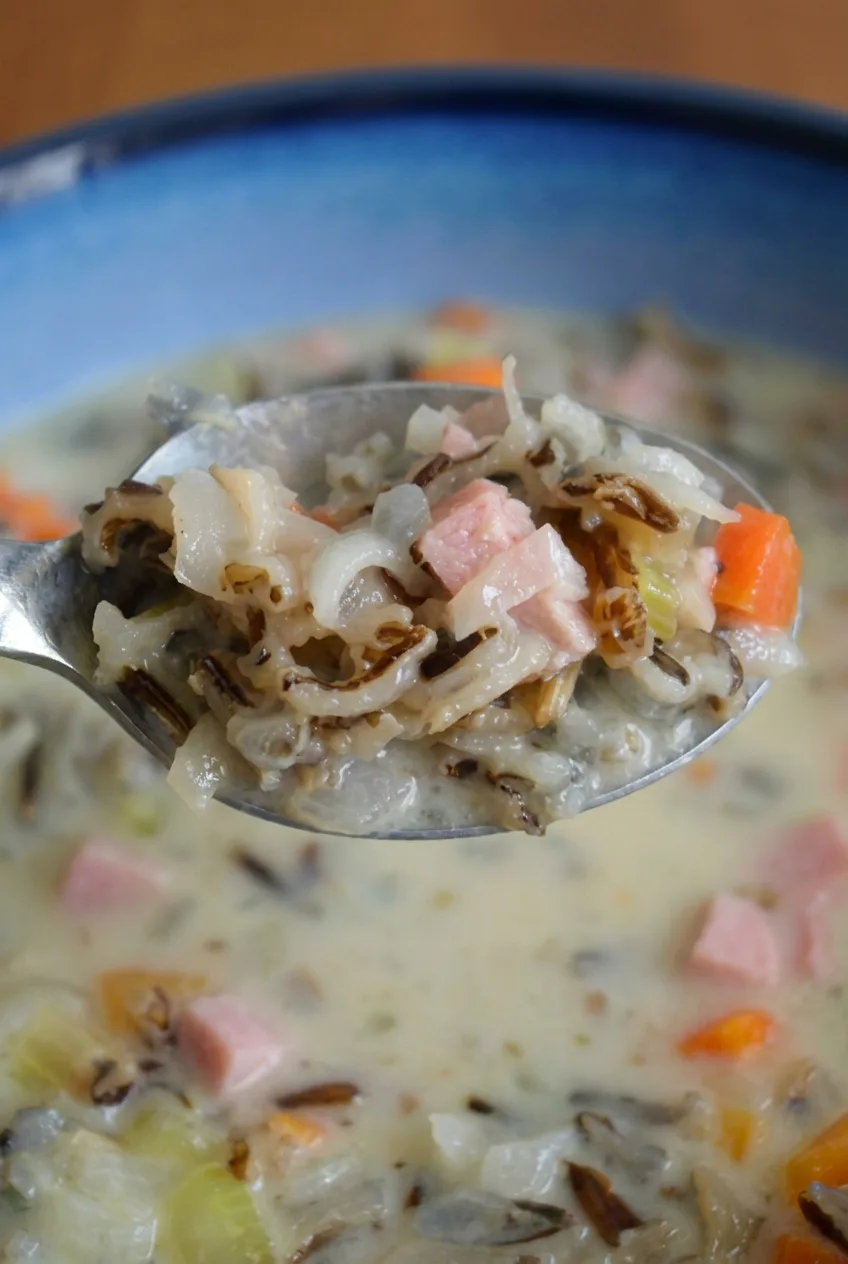 Close view of creamy ham wild rice soup showing split dark rice, diced ham, carrots, celery, and onion.