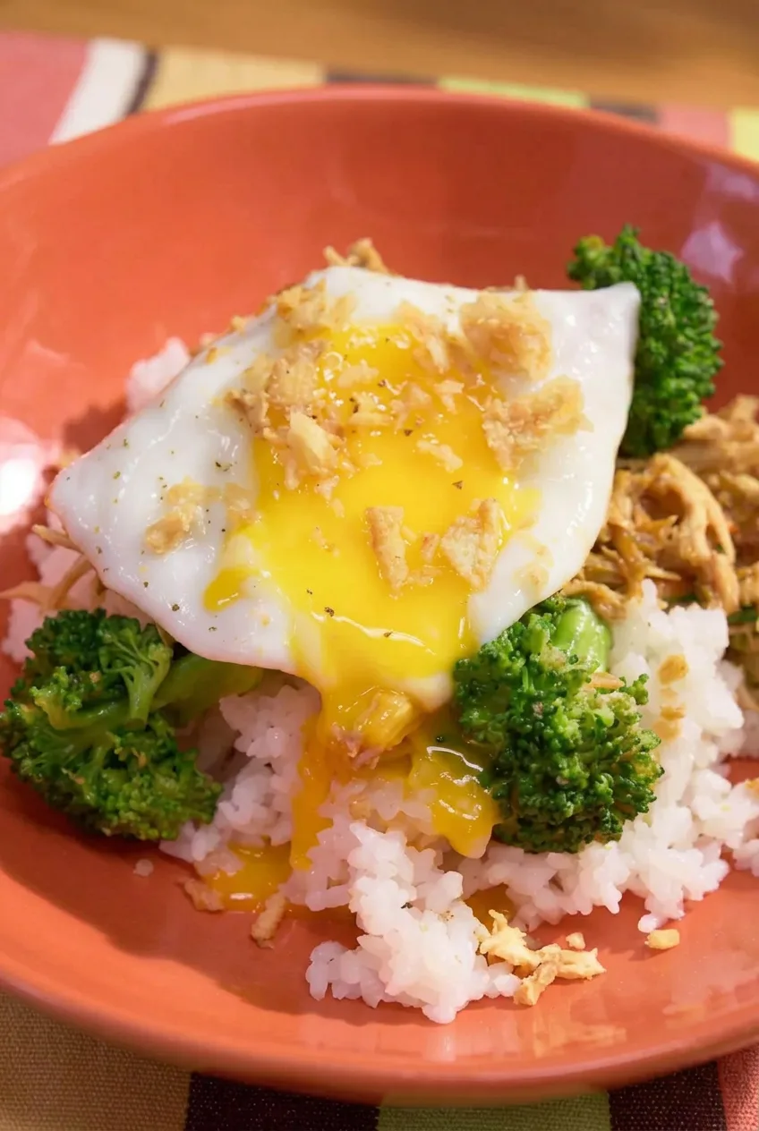 Soft egg yolk running over white rice beside teriyaki chicken and broccoli