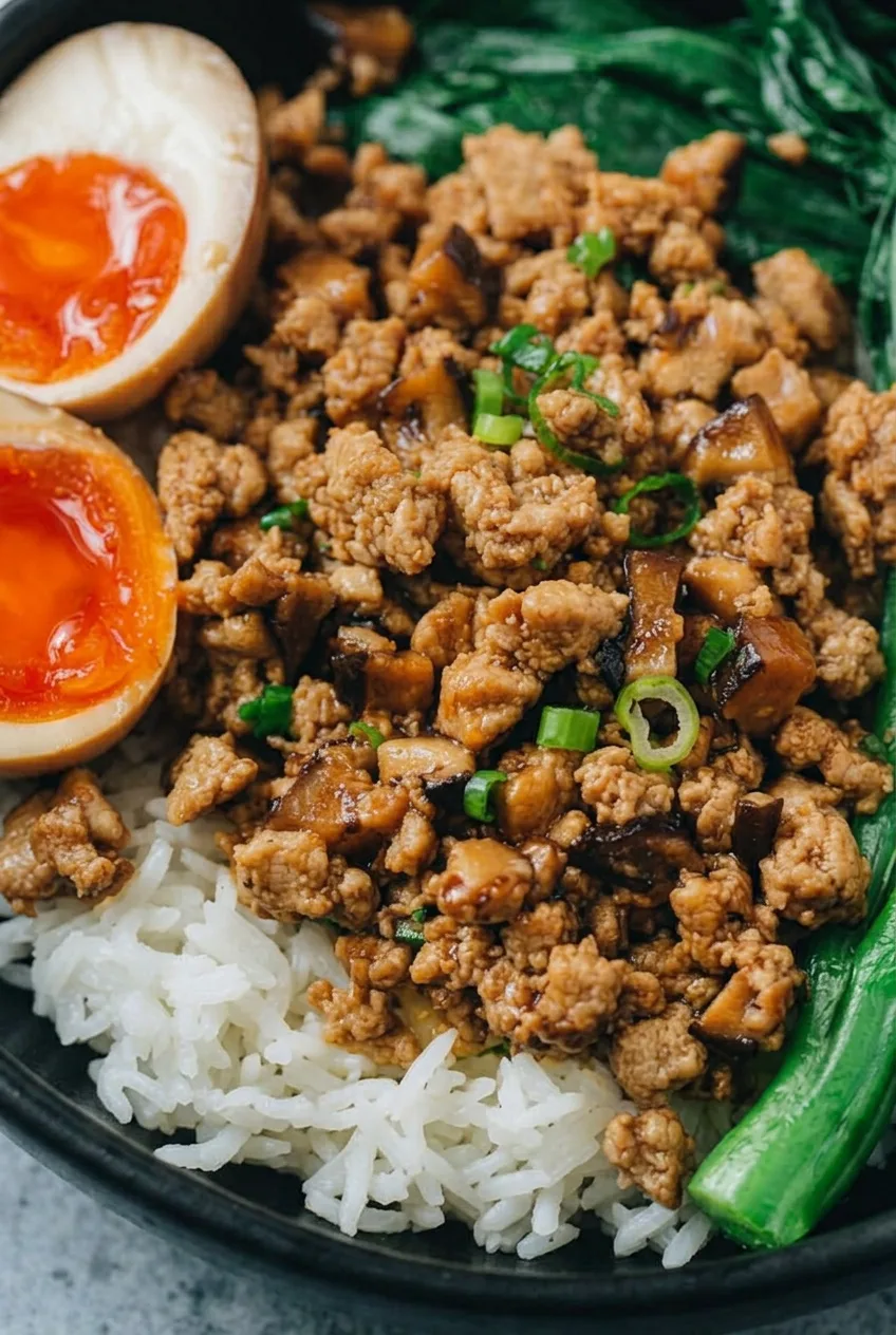 Close view of glossy chicken and mushroom crumbles beside white rice and a soft orange egg yolk