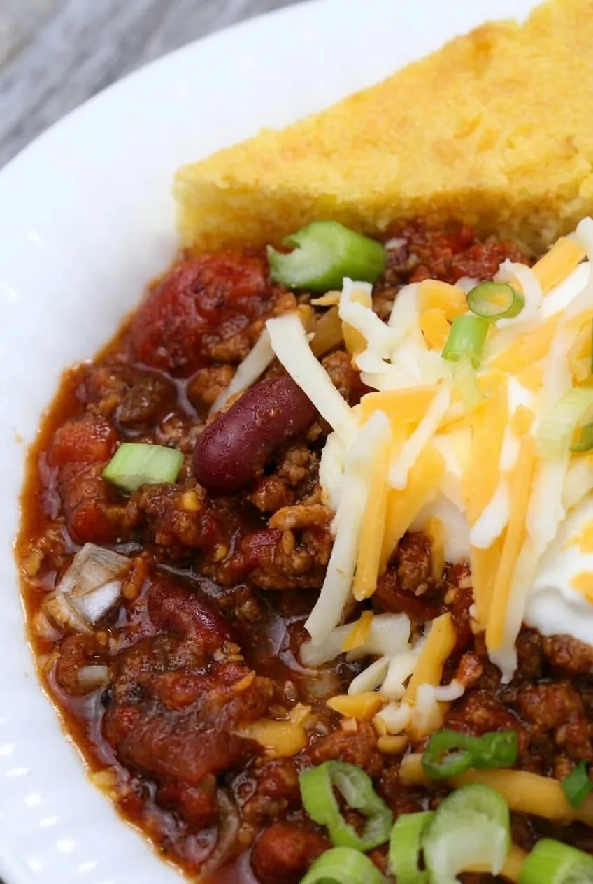 Close view of thick turkey chili with kidney beans, tomato pieces, cheese, sour cream, and green onions