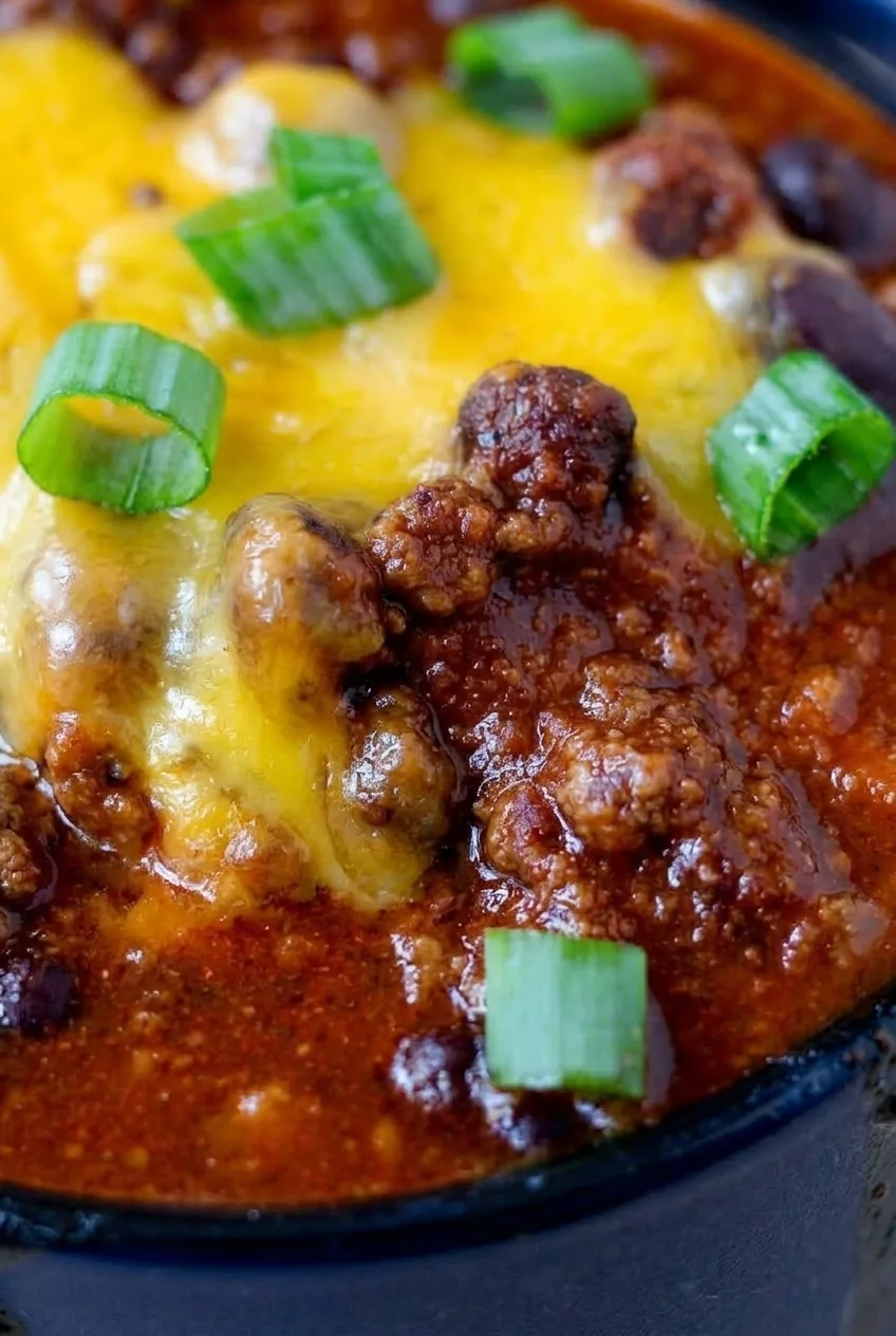 Close view of beef crumbles and dark beans in thick chili beneath melted cheddar and green onions