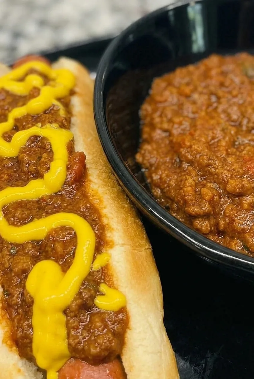 Close view of finely crumbled beef chili clinging to a hot dog beneath yellow mustard