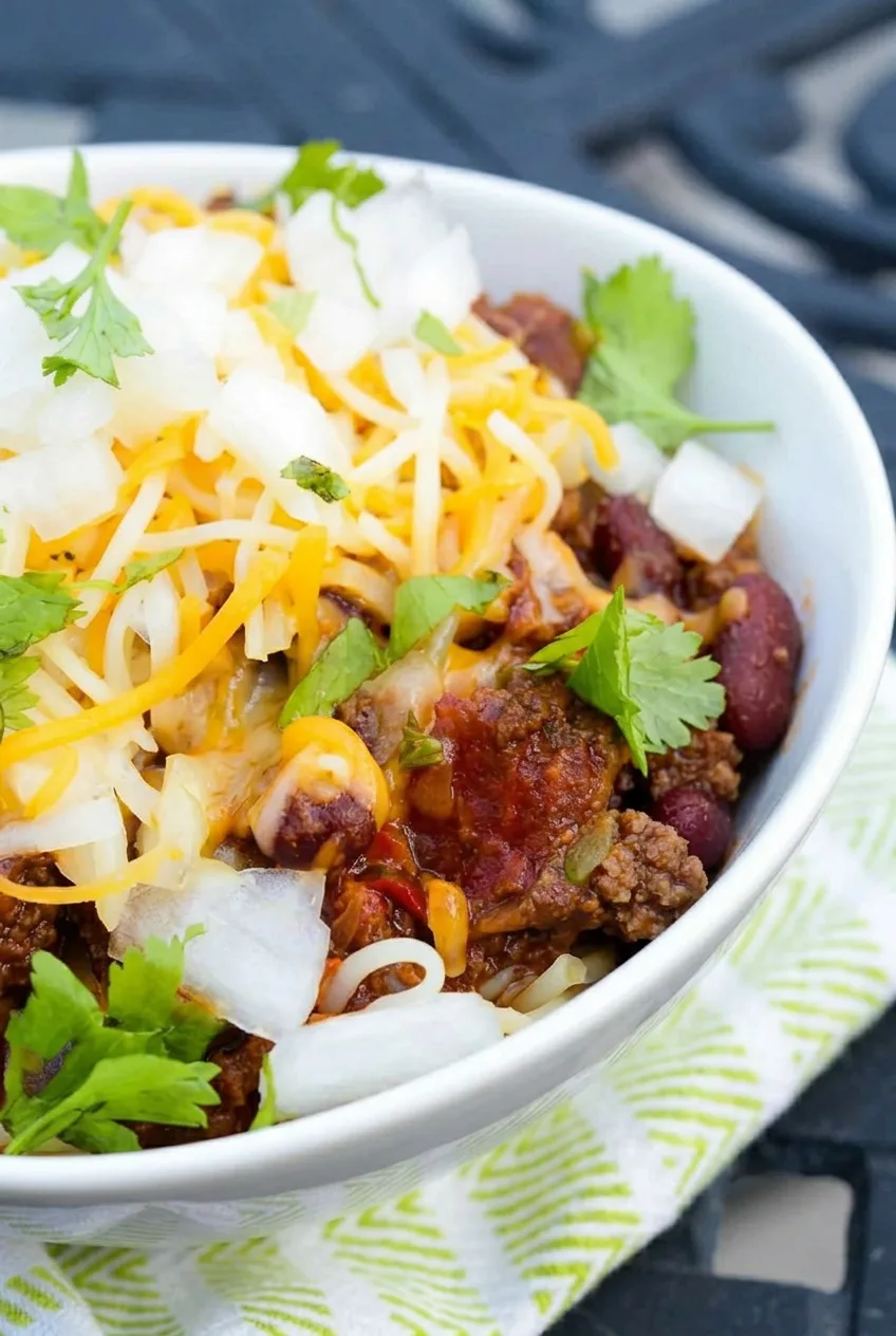 Close view of beef crumbles and kidney beans in Cincinnati chili beneath cheese, onion, and cilantro