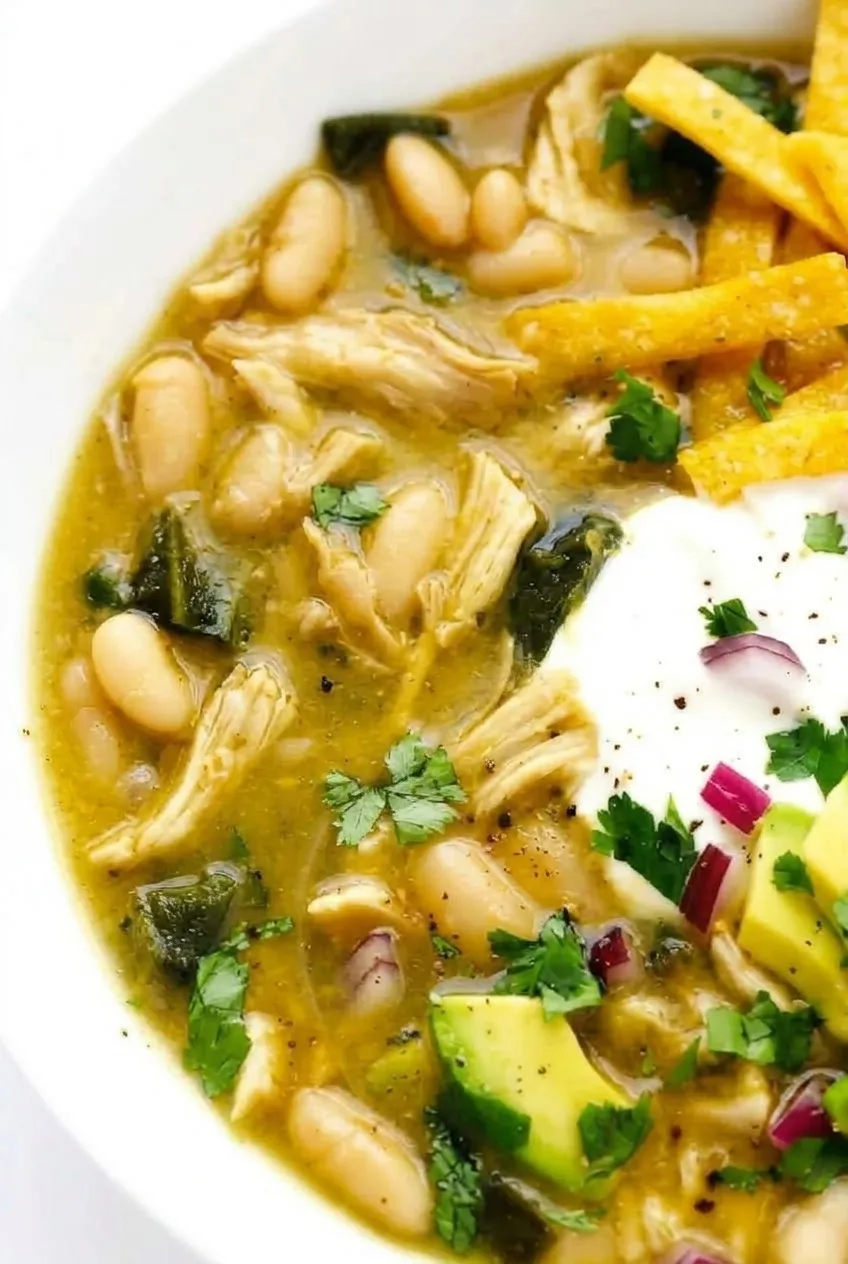 Close view of chicken shreds, whole white beans, and poblano pieces in golden-green chili broth