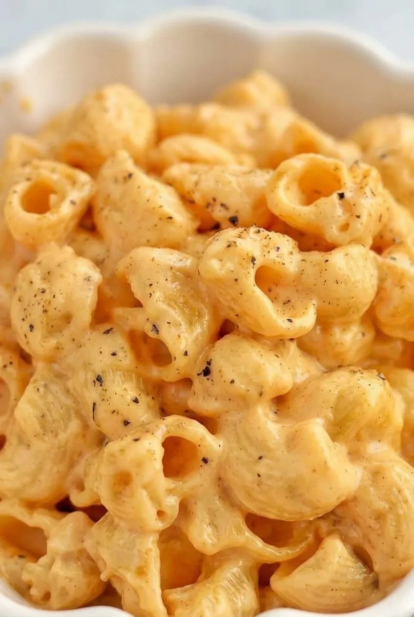 Close view of hollow elbow macaroni coated in glossy cheese sauce and flecked with black pepper