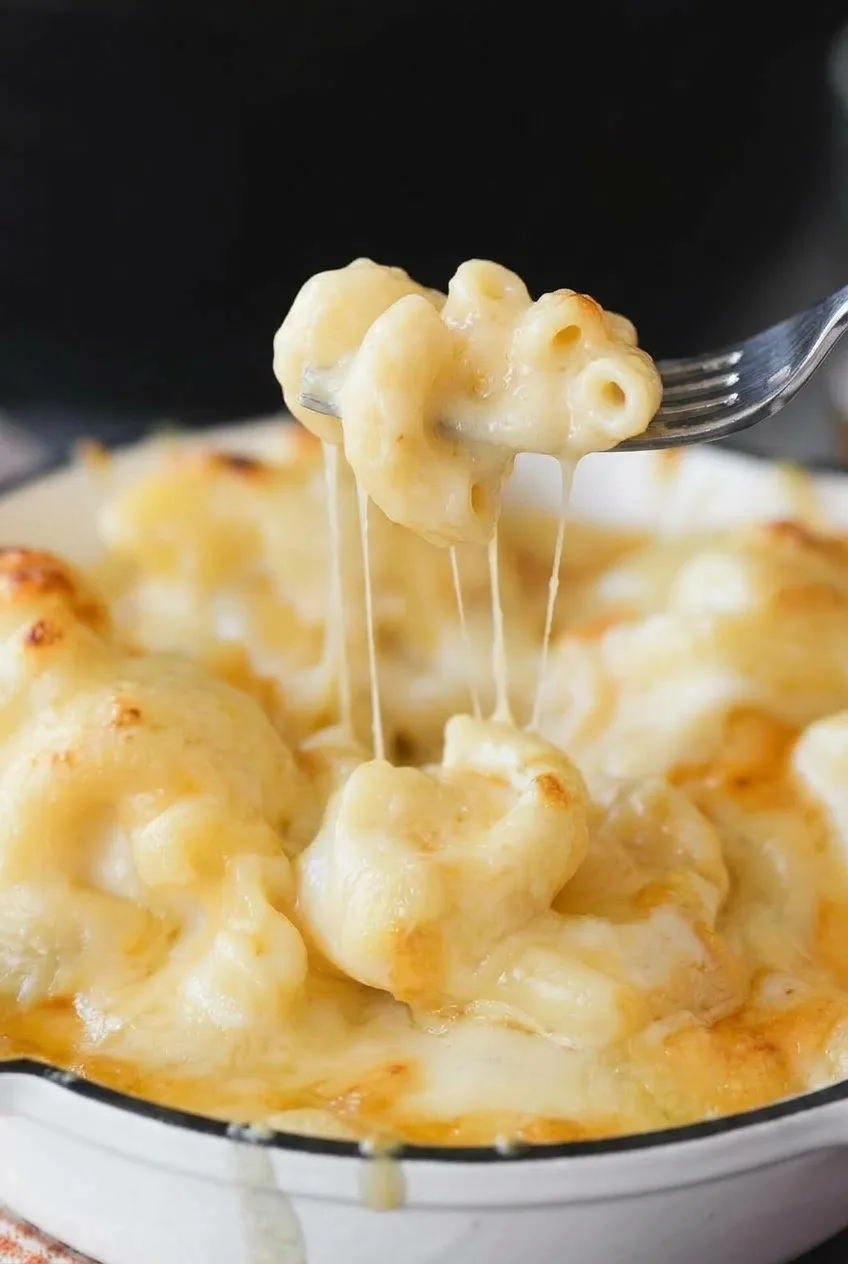 Close view of saucy elbow macaroni and melted cheese stretching from a lifted forkful