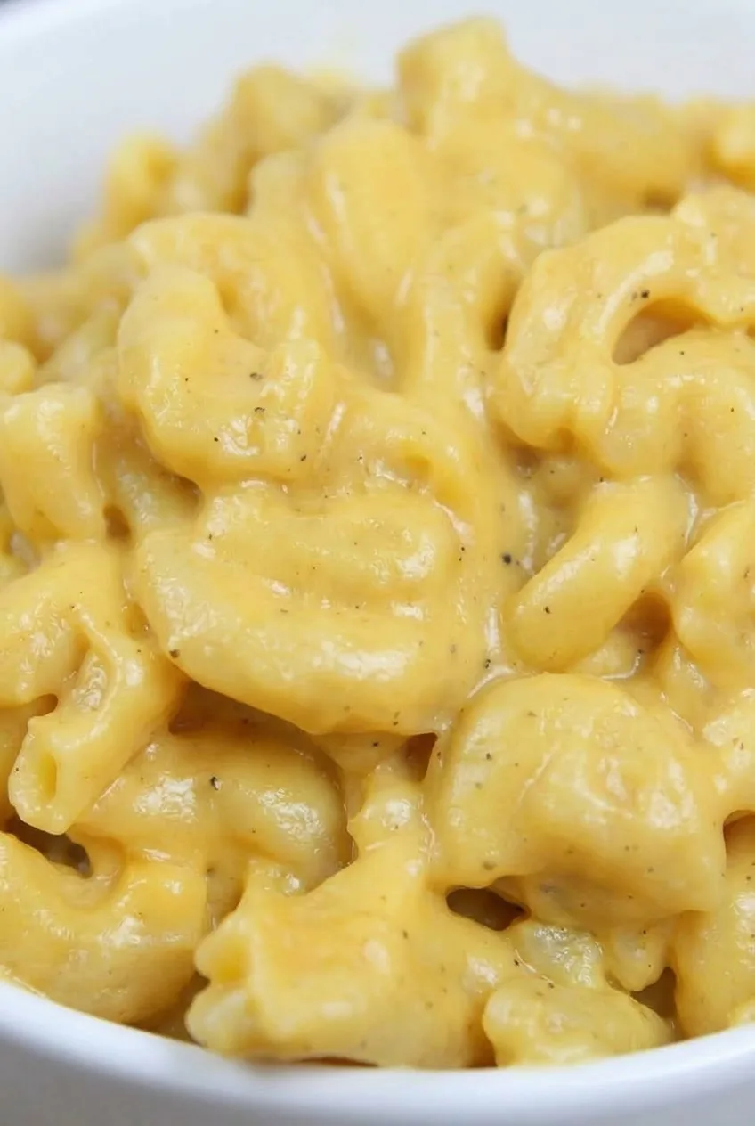 Close view of intact elbow macaroni coated in creamy golden cheese sauce