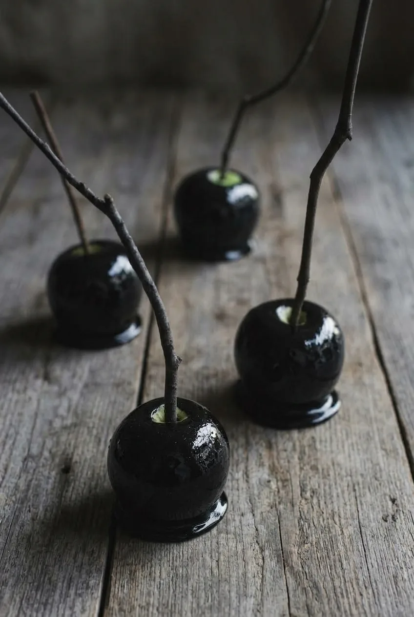 Several glossy black poison candy apples spaced across a dark rustic serving surface.