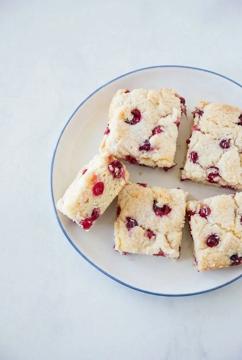 Overhead view of several thick cranberry breakfast cake squares with whole berries and coarse sugar topping.