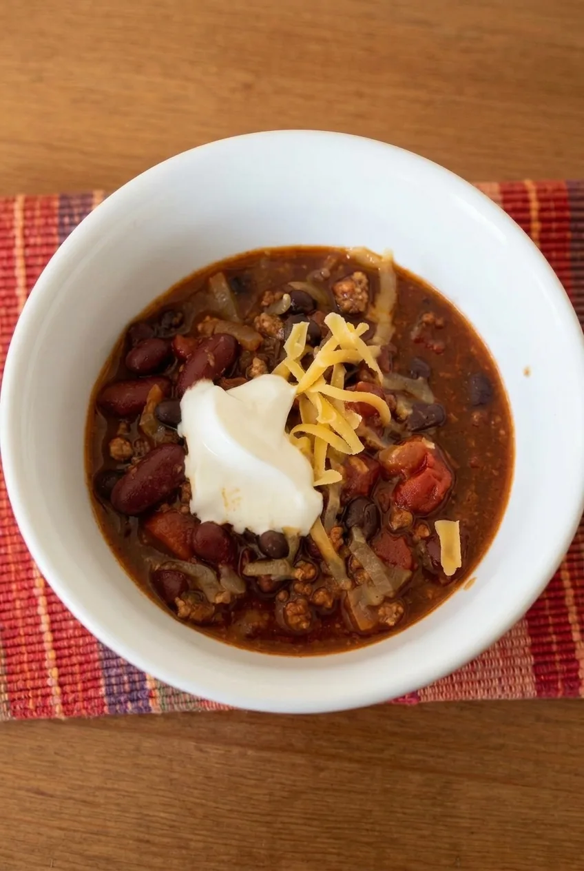 Complete bowl of ground turkey chili with sour cream and cheddar on a warm tabletop