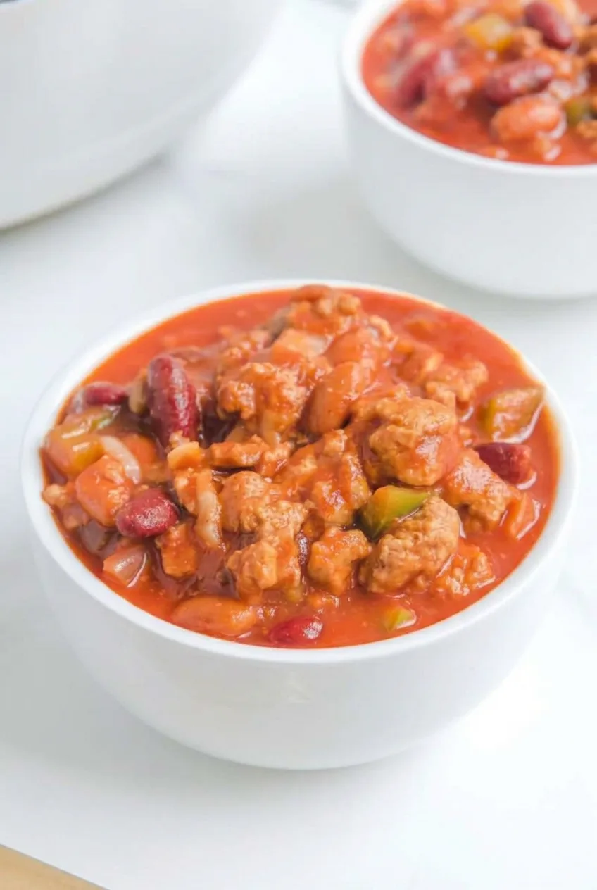 Complete white bowl of ungarnished beef-and-bean chili on a pale tabletop