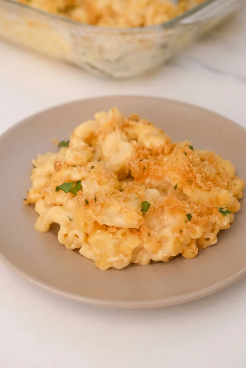 Full plate of creamy baked Velveeta mac and cheese with a casserole dish softly visible behind it