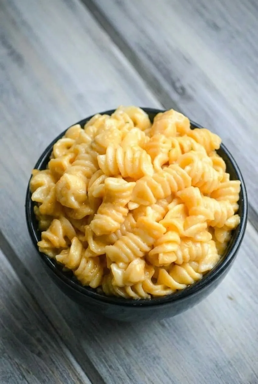 Full dark bowl of rotini mac and cheese on a gray wooden tabletop