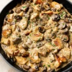 Creamy chicken stroganoff with browned mushrooms and parsley in a dark skillet
