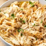 Crockpot Italian chicken in a shallow white bowl, with distinct golden-tan shreds and scattered parsley