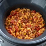 Crock Pot goulash with elbow macaroni, ground beef, and chunky tomatoes in an open slow cooker