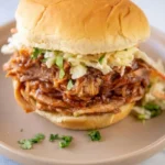Crock Pot BBQ pulled pork sandwich with pale coleslaw layered beneath a soft golden bun