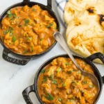 Two dark bowls of slow cooker butter chicken with cauliflower and cilantro, served beside toasted naan.