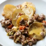 Crockpot hobo casserole scooped onto a light plate with potato rounds, ground beef, carrots, and melted cheddar