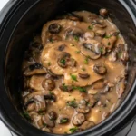 Whole Crock Pot Chicken Marsala breasts with sliced mushrooms and parsley in a black slow cooker
