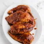Whole Slow Cooker Coca Cola Chicken breasts coated in glossy barbecue sauce on a white plate